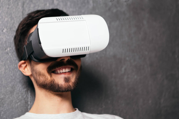 Крупным планом портрет молодого улыбающегося мужчины носит VR гарнитуру. Бородатый мужчина в очках виртуальной реальности, играющий в видеоигры, с открытым ртом. Концепция технологии будущего. Гаджет виртуальной жизни. - Фото, изображение