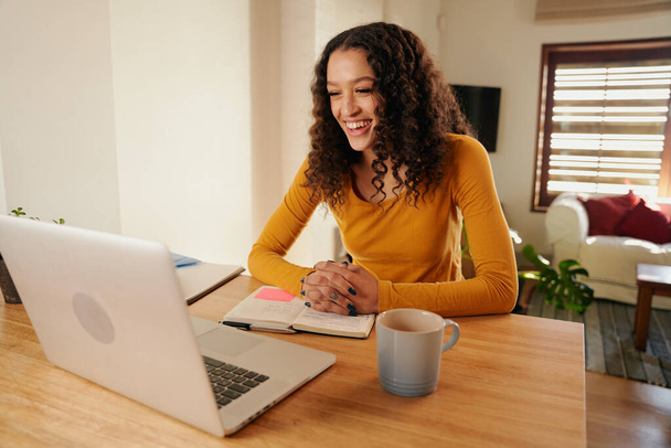 Çevrimiçi toplantıda çok kültürlü bir kadın gülüyor. Modern dairede dizüstü bilgisayarla çalışan genç profesyonel uzaktan kumanda. - Fotoğraf, Görsel