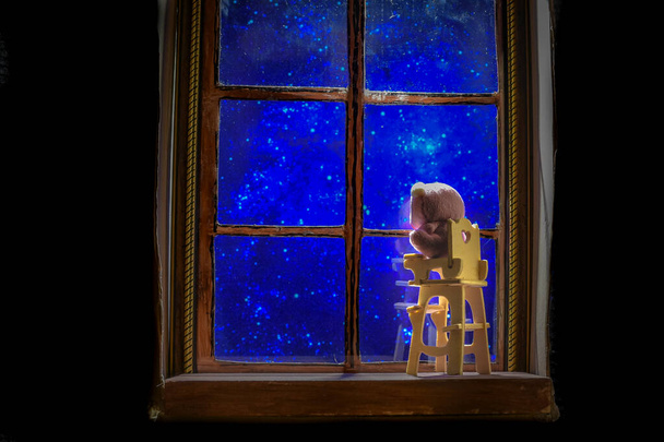 mecedora infantil contra el fondo del cielo estrellado fuera de la ventana por la noche - Foto, imagen