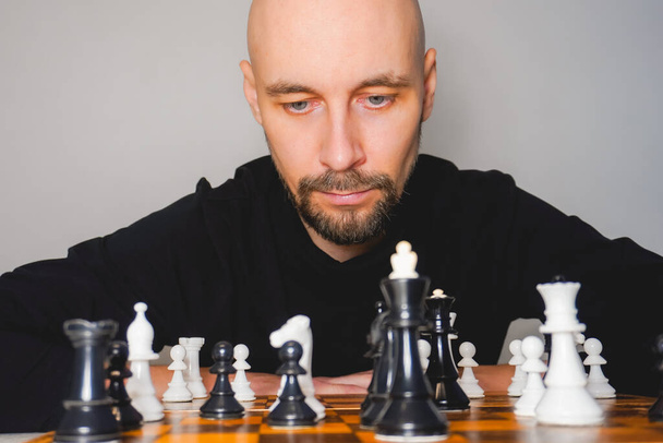 Thoughtful bald man wearing beard playing chess on board. Strategy and competition concept. Selective focus - Фото, изображение