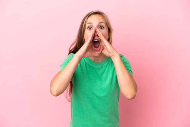 Nuori Englanti nainen eristetty vaaleanpunainen tausta huutaa ja ilmoittaa jotain - Valokuva, kuva