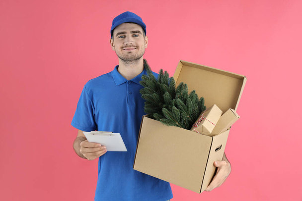 Entrega hombre con cajas y portapapeles sobre fondo rosa, concepto de Navidad - Foto, imagen