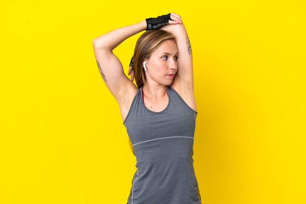 Young English woman isolated on yellow background stretching - Photo, Image