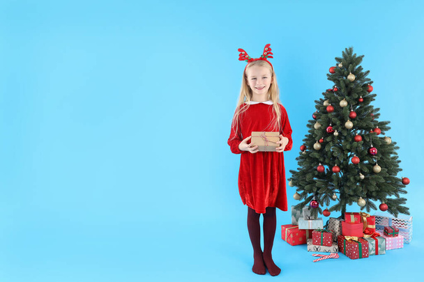 Cute little girl on blue background with Christmas tree and gifts - Fotoğraf, Görsel