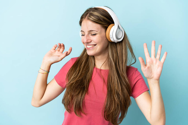 Молодая белая женщина, изолированная на синем фоне, слушает музыку и танцует - Фото, изображение
