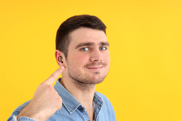 Young man with hearing aid on yellow background - Photo, Image
