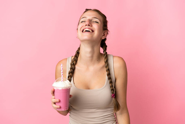 Νεαρή γυναίκα με μιλκσέικ φράουλα απομονωμένη σε ροζ φόντο γελώντας - Φωτογραφία, εικόνα