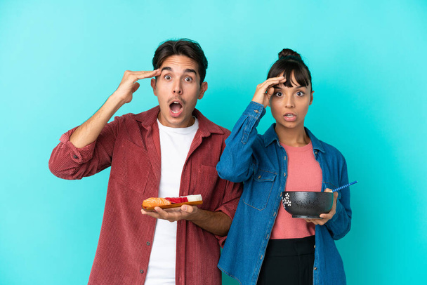 Young mixed race friends holding sashimi and ramen isolated on blue background has just realized something and has intending the solution - Photo, Image