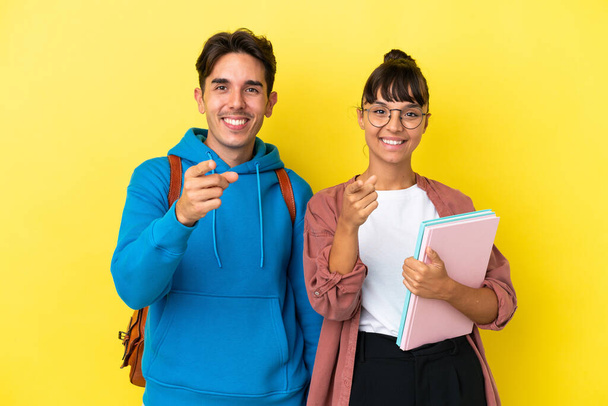 Jeune couple étudiant isolé sur fond jaune pointe du doigt vers vous avec une expression confiante - Photo, image