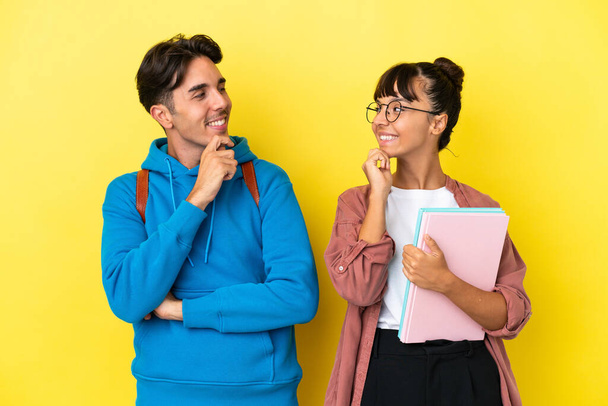 Young student couple isolated on yellow background looking looking at each other - Photo, Image