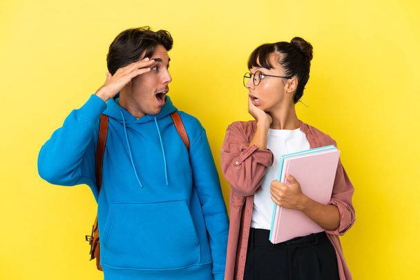 Giovane coppia di studenti isolato su sfondo giallo con sorpresa e scioccato espressione facciale - Foto, immagini