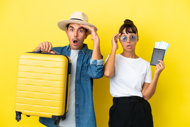 Νέοι ταξιδιώτες φίλοι κρατώντας μια βαλίτσα και διαβατήριο που απομονώνονται σε κίτρινο φόντο έχει μόλις συνειδητοποιήσει κάτι και έχει την πρόθεση της λύσης - Φωτογραφία, εικόνα