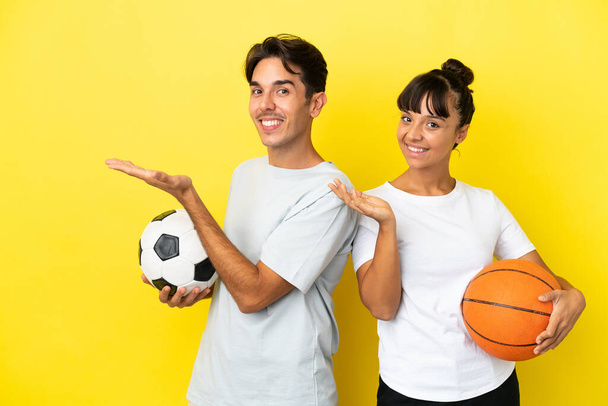 young sport couple playing football and basketball isolated on yellow background pointing back and presenting a product - Foto, Imagem