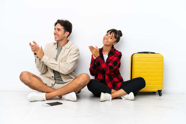 Jovens viajantes mestiços casal sentado no chão isolado no fundo branco aplaudindo após a apresentação em uma conferência - Foto, Imagem