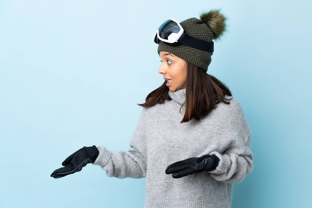 Snowboard gözlüklü karışık kayakçı kız mavi arka planda sürpriz bir ifadeyle yan yana bakarken. - Fotoğraf, Görsel