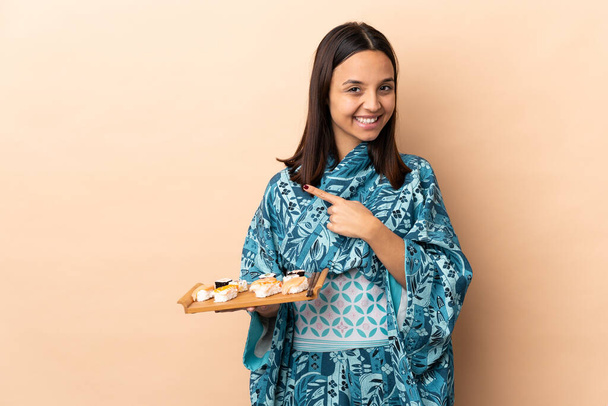 Woman wearing kimono and holding sushi over isolated background pointing to the side to present a product - Foto, Imagem