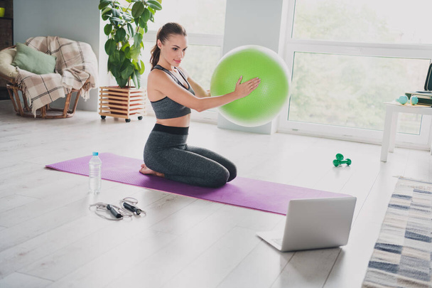 Portrait of attractive sportive girl doing yoga stretching holding ball watching video at light home indoors - Photo, Image