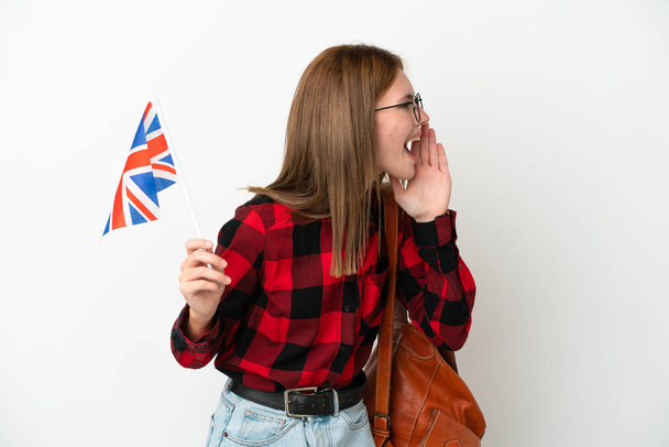 Junge Frau mit einer britischen Flagge auf blauem Hintergrund, die mit weit geöffnetem Mund zur Seite schreit - Foto, Bild