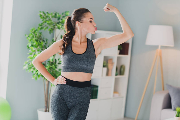 Photo of confident cool lady wear sport outfit kissing arm muscles indoors home house - Foto, afbeelding