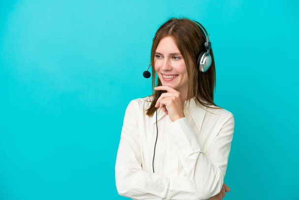 Telemarketer English woman working with a headset isolated on blue background looking to the side - Φωτογραφία, εικόνα