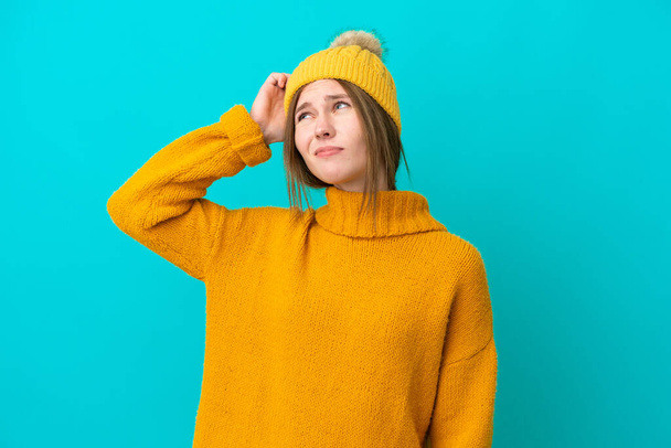 Jeune femme anglaise vêtue d'une veste d'hiver isolée sur fond bleu ayant des doutes et avec une expression du visage confuse - Photo, image