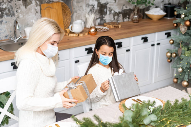 Beautiful mother and daughter in medical masks have fun at home near the Christmas tree in a interior. Family happiness, holiday, joy, vacation, games with a woman. New Years preparations - Photo, Image