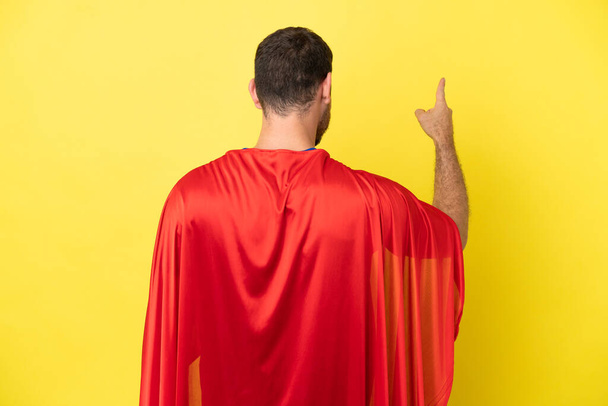Super Hero Brazilian man isolated on yellow background pointing back with the index finger - Photo, image
