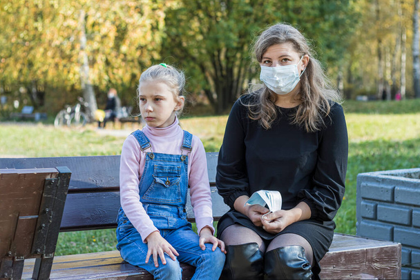 on the street. mom sits on a bench and puts on a medical mask for the child. sunny day. - Photo, Image