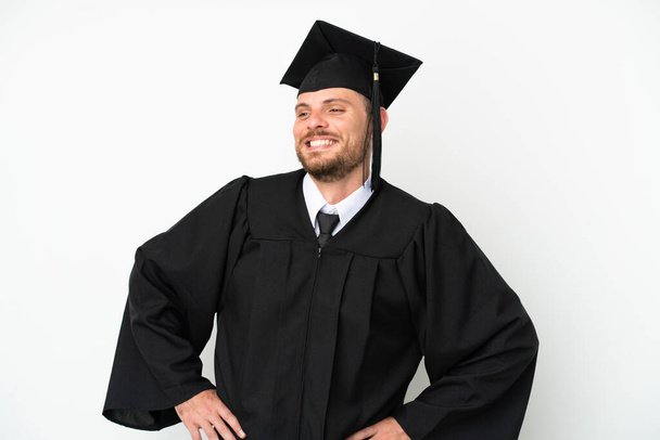młody uniwersytet Brazylijski absolwent izolowany na białym tle pozowanie z ramionami na biodrze i uśmiechnięty - Zdjęcie, obraz