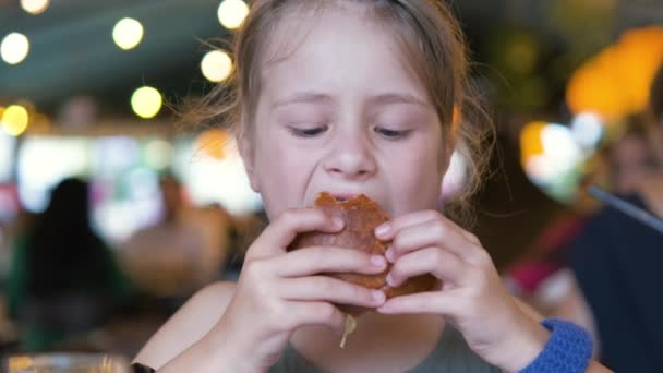 Dziecko dziewczyna jedzenie smaczny burger w restauracji - Materiał filmowy, wideo