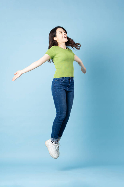 Portrait of beautiful young asian girl jumping up, isolated on blue background - Valokuva, kuva