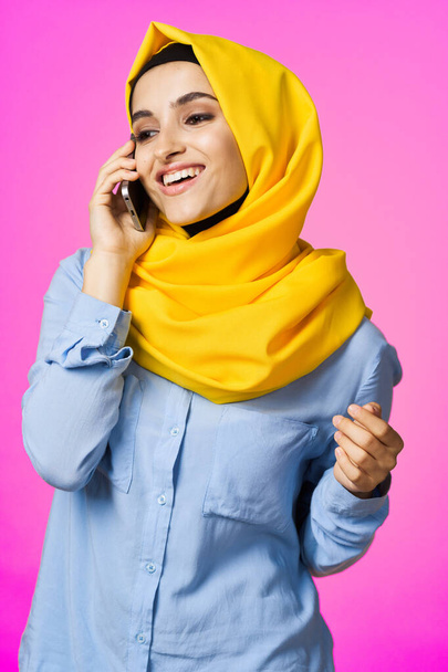 Sarı tesettürlü müslüman kadın telefonda pembe teknolojiyle konuşuyor. - Fotoğraf, Görsel