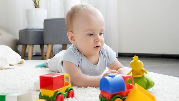 Little baby boy playing with colorful toy cars on carpet in living room. Concept of children development, education and creativity at home - Photo, Image