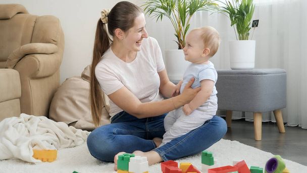 Cute smiling baby boy sitting on mothers lap and looking on colorful toys. Concept of children development, education and creativity at home - Φωτογραφία, εικόνα