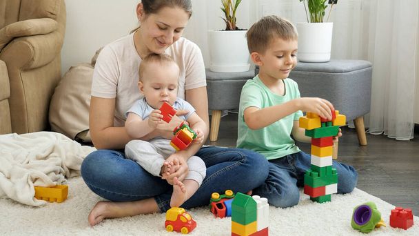 Bambini felici con madre che gioca sul tappeto e costruisce una torre giocattolo. Concetto di famiglia che ha tempo insieme e sviluppo dei bambini - Foto, immagini