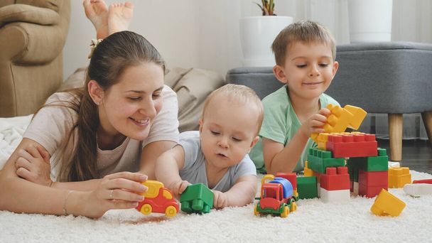 Iloinen hymyilevä perhe nauttii lelujen pelaamisesta ja hauskanpidosta matolla yhdessä kotona. Käsitys perheen yhteisestä ajasta ja lasten kehityksestä - Valokuva, kuva