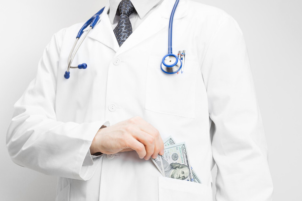 Doctor putting money into his pocket with his left hand - Фото, изображение