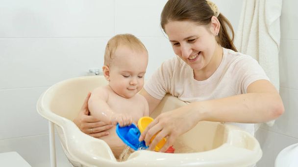 Cheerful smiling baby with mother playing while washing in bath. Concept of children hygiene, healthcare and parenting. - Photo, Image