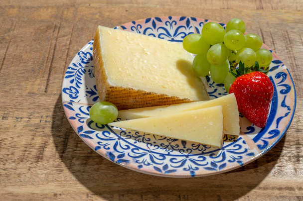 チーズコレクション、羊乳から作られたラ・マンチャ地方のスパニッシュハードマンチェゴチーズ、緑のブドウと赤いイチゴのクローズアップ - 写真・画像