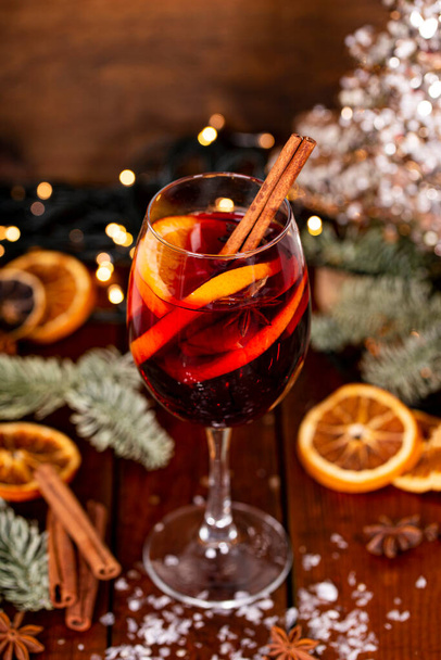 A glass of mulled wine on the wooden table surrounded by Christmas decorations. Festive winter drink vertical photo - Zdjęcie, obraz