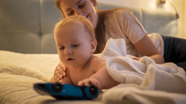 Cute baby boy crawling away from mother on bed at night. Concept of parenting, child development and family having time together. - Фото, зображення