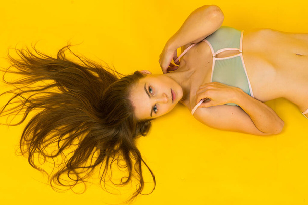 Czarująca kobieta z uwodzicielskim ciałem i dużymi piersiami w bieliźnie na niebiesko żółtym tle studio - Zdjęcie, obraz
