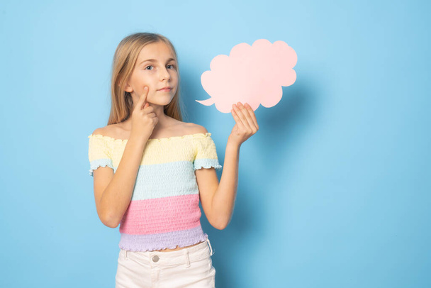 Θλιβερό κοριτσάκι με καλοκαιρινά ρούχα που δείχνει χάρτινο σύννεφο πάνω από μπλε φόντο. - Φωτογραφία, εικόνα