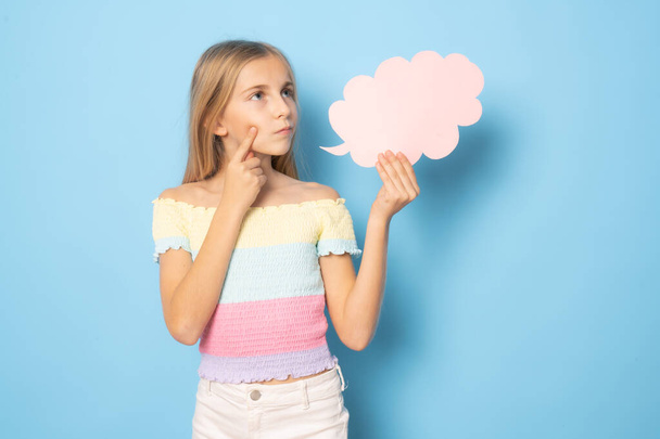 Страшная маленькая девочка в летней одежде показывает бумажное облако на синем фоне. - Фото, изображение