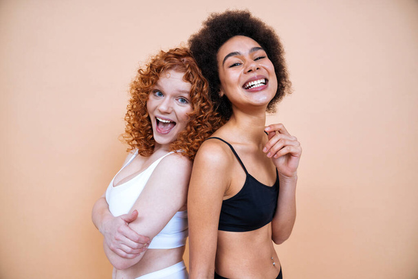 beauty image of two young women with different skin and body posing in studio for a body positive photoshooting. Mixed female models in lingerie on colored backgrounds - Zdjęcie, obraz
