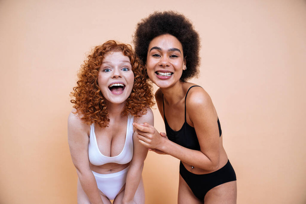 beauty image of two young women with different skin and body posing in studio for a body positive photoshooting. Mixed female models in lingerie on colored backgrounds - Foto, Bild