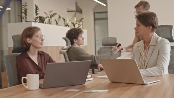 Powolne ujęcie zespołu męskich i żeńskich kolegów pracujących nad wspólnym projektem, siedzących razem przy laptopach przy stole w nowoczesnym biurze - Materiał filmowy, wideo