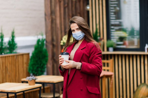 Közelkép egy orvosi maszkot viselő fehér nőről, aki az utcán és egy kávézóban áll. - Fotó, kép