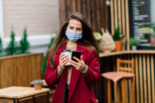 Ritratto ravvicinato di una donna caucasica con una maschera medica e in piedi in strada e di un caffè - Foto, immagini