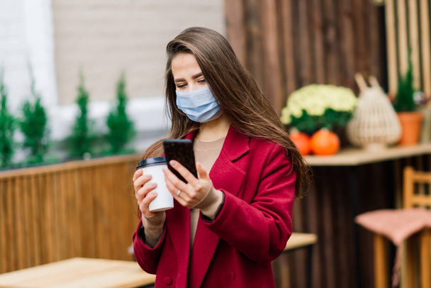 Retrato de cerca de una mujer caucásica con una máscara médica y de pie en la calle y de un café - Foto, Imagen
